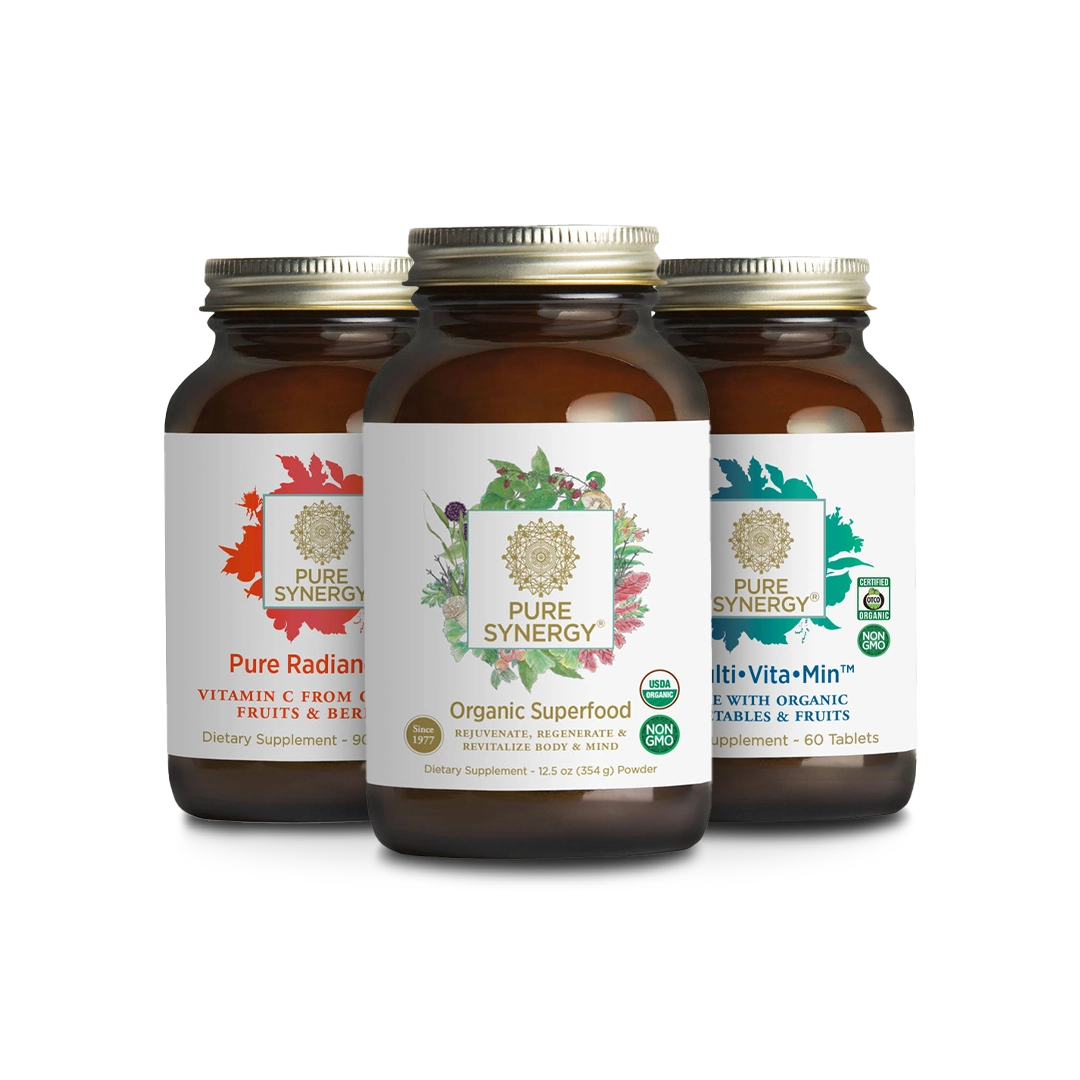 Three brown bottles of Pure Synergy dietary supplements are displayed. The bottles are labeled Pure Radiance, Organic Superfood, and Multi Vita•Min. Each has colorful designs representing different ingredients and benefits.
