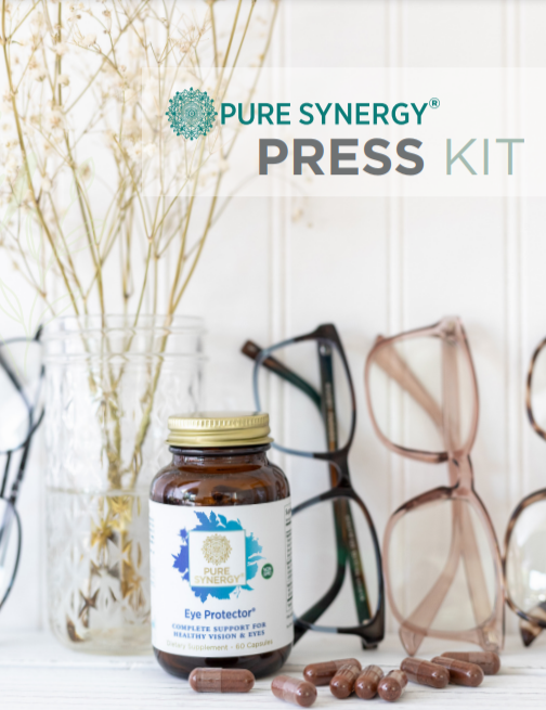 A bottle of Pure Synergy Eye Protector supplements is on a white surface with a few capsules scattered next to it. Behind, several pairs of eyeglasses are displayed, and a glass jar holds delicate dried flowers.